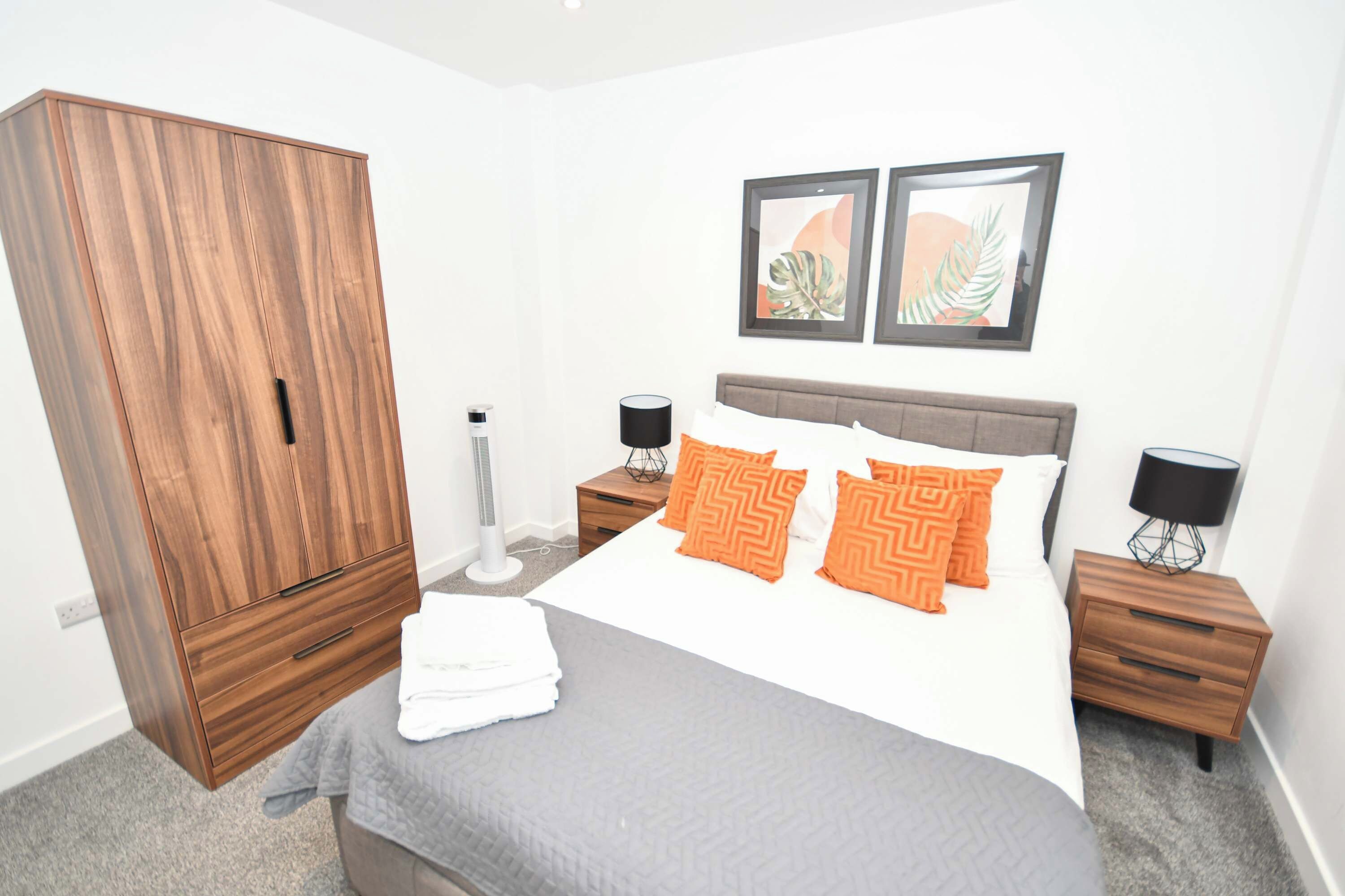 A bedroom with a bed, nightstands, a wardrobe, and two wall-mounted pictures.