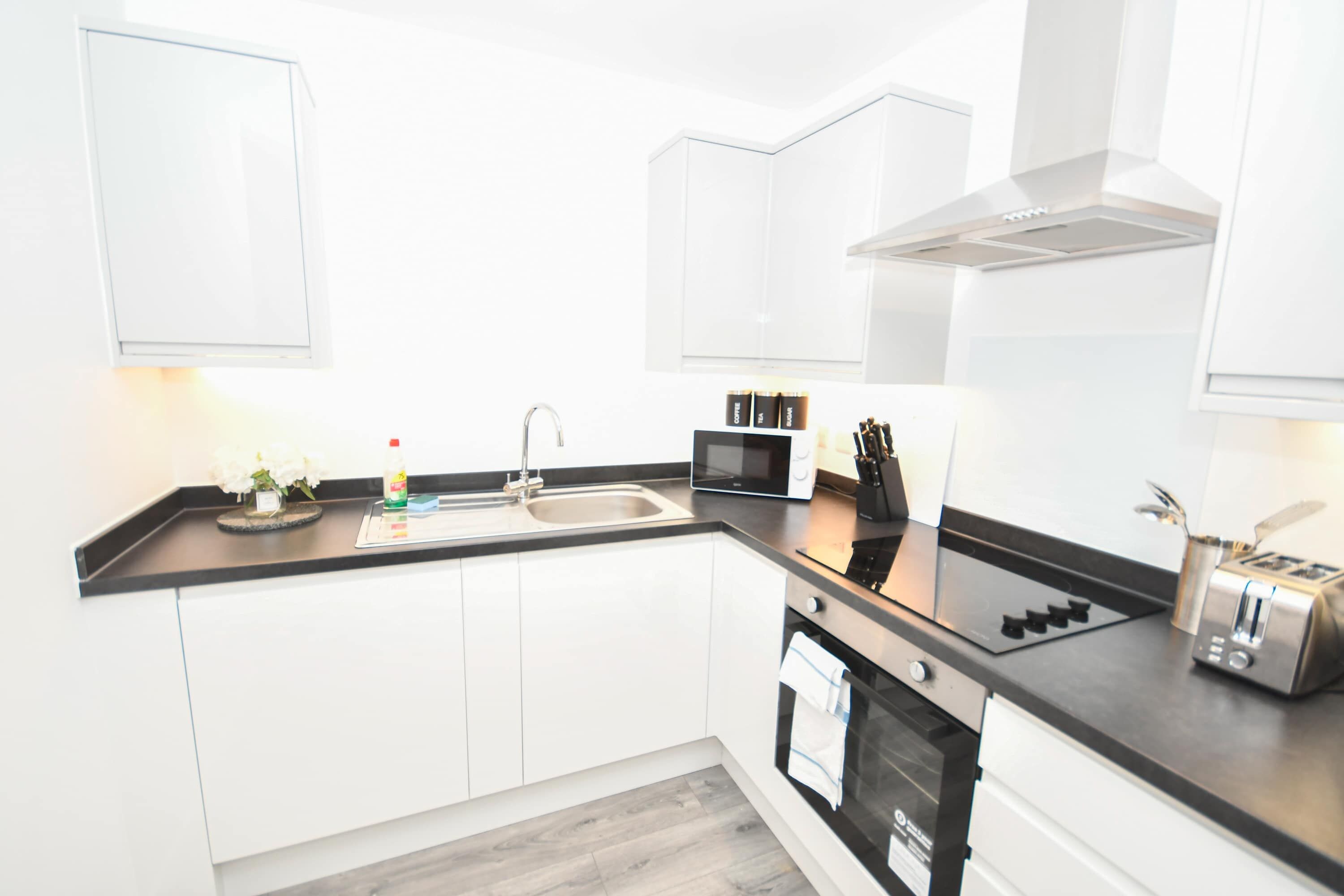 A modern kitchen with white cabinets, a black countertop, a sink, a microwave, a toaster, and a stove.