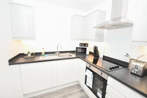 A modern kitchen with white cabinets, a black countertop, a sink, a microwave, a toaster, and a stove. - Lovely 1 Bedroom Apartment in Leeds w WiFi (Leeds)