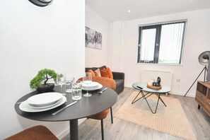 Ein modernes Wohnzimmer mit Essbereich, ausgestattet mit einem runden Tisch, einer Couch, einem kleinen Couchtisch und einer Topfpflanze.