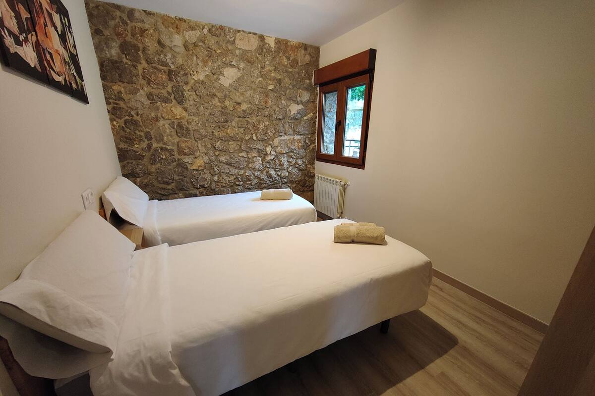 A room with two beds, a stone wall, a radiator, and a window with a view.