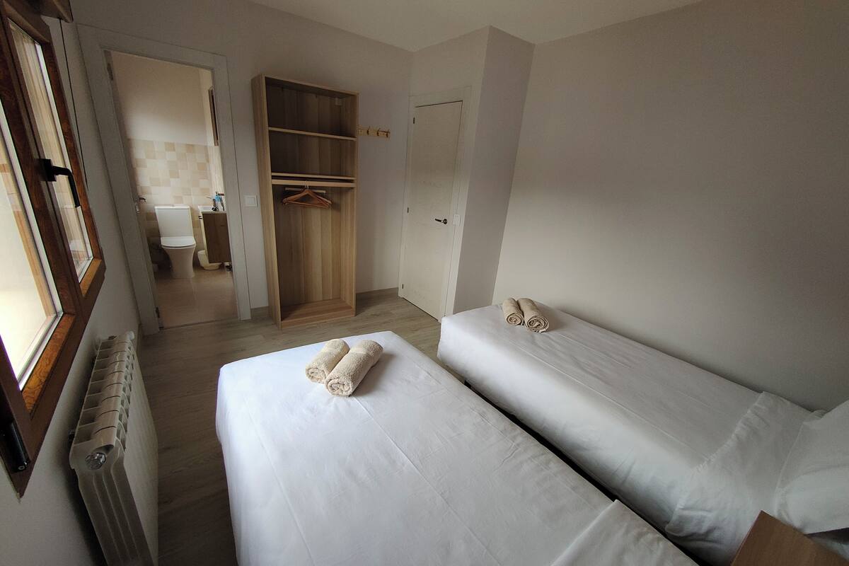 A hotel room with two beds, a wooden wardrobe, a bathroom, and a radiator.