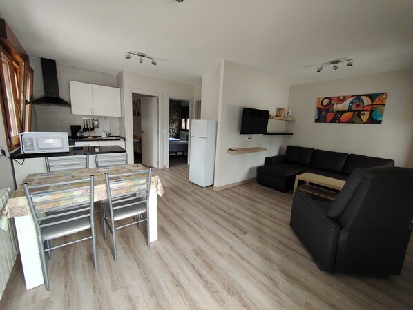 A modern living space with a dining area, kitchen, and a black leather sofa.