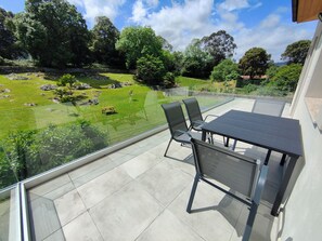 A balcony with a glass railing, a table, and chairs.