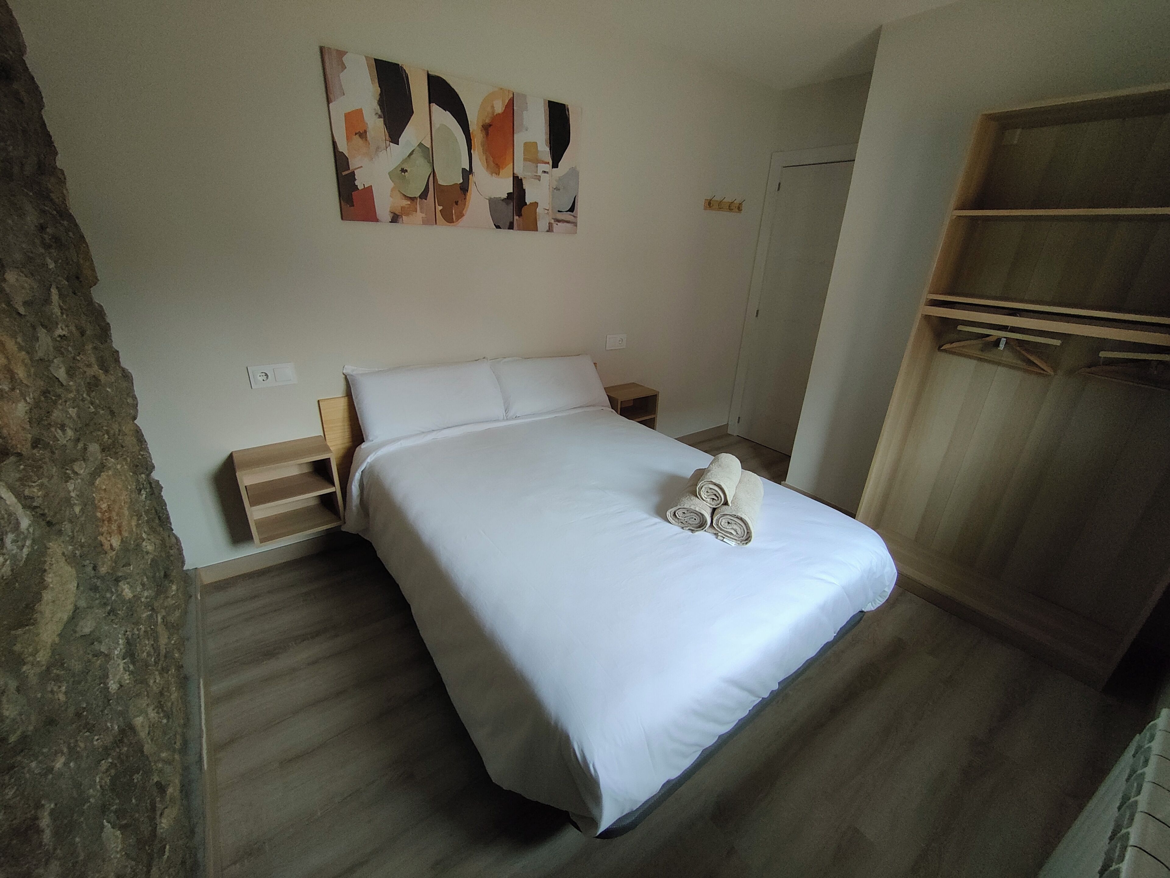 A bedroom with a bed, a wooden nightstand, a wardrobe, and a wall-mounted abstract art piece.