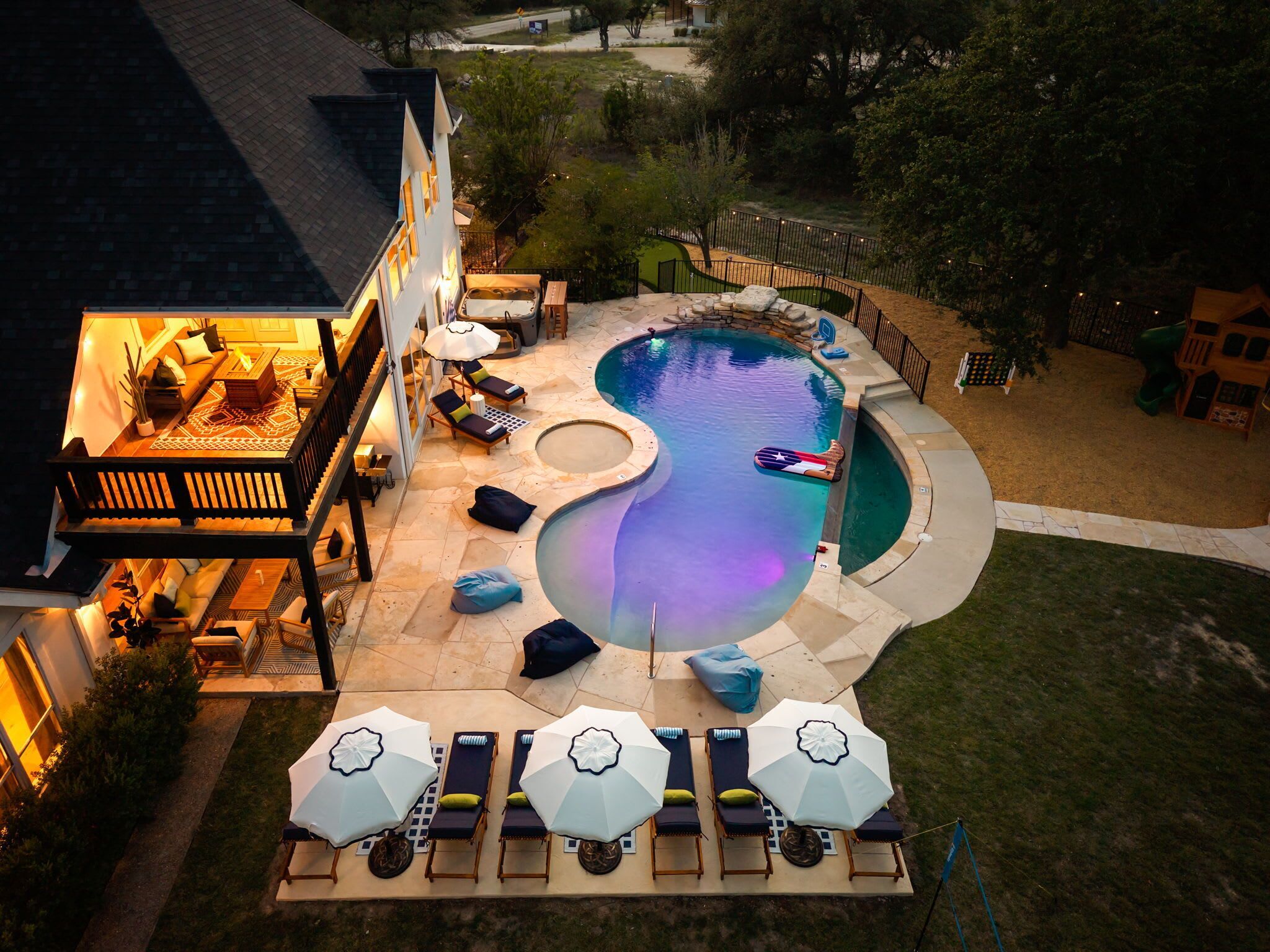 A swimming pool with a hot tub, lounge chairs, and umbrellas.