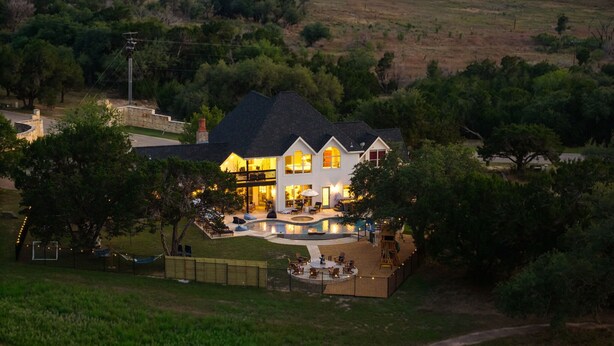 Un'ampia casa con piscina, immersa tra alberi e un paesaggio collinare.