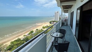 Un balcon avec vue sur la plage et l’océan, une table avec des chaises et un bâtiment en arrière-plan.