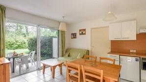 A room with a dining table, chairs, a sofa, a refrigerator, and a sliding glass door leading to a garden. - Accessible Vineyard Stay for Four (Rivieres)