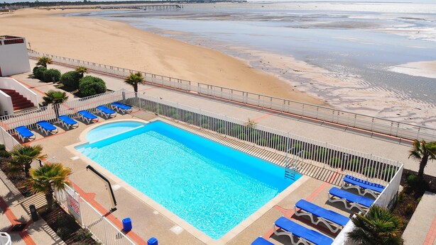 Una piscina con sillas de descanso, vista al mar y un muelle a lo lejos.