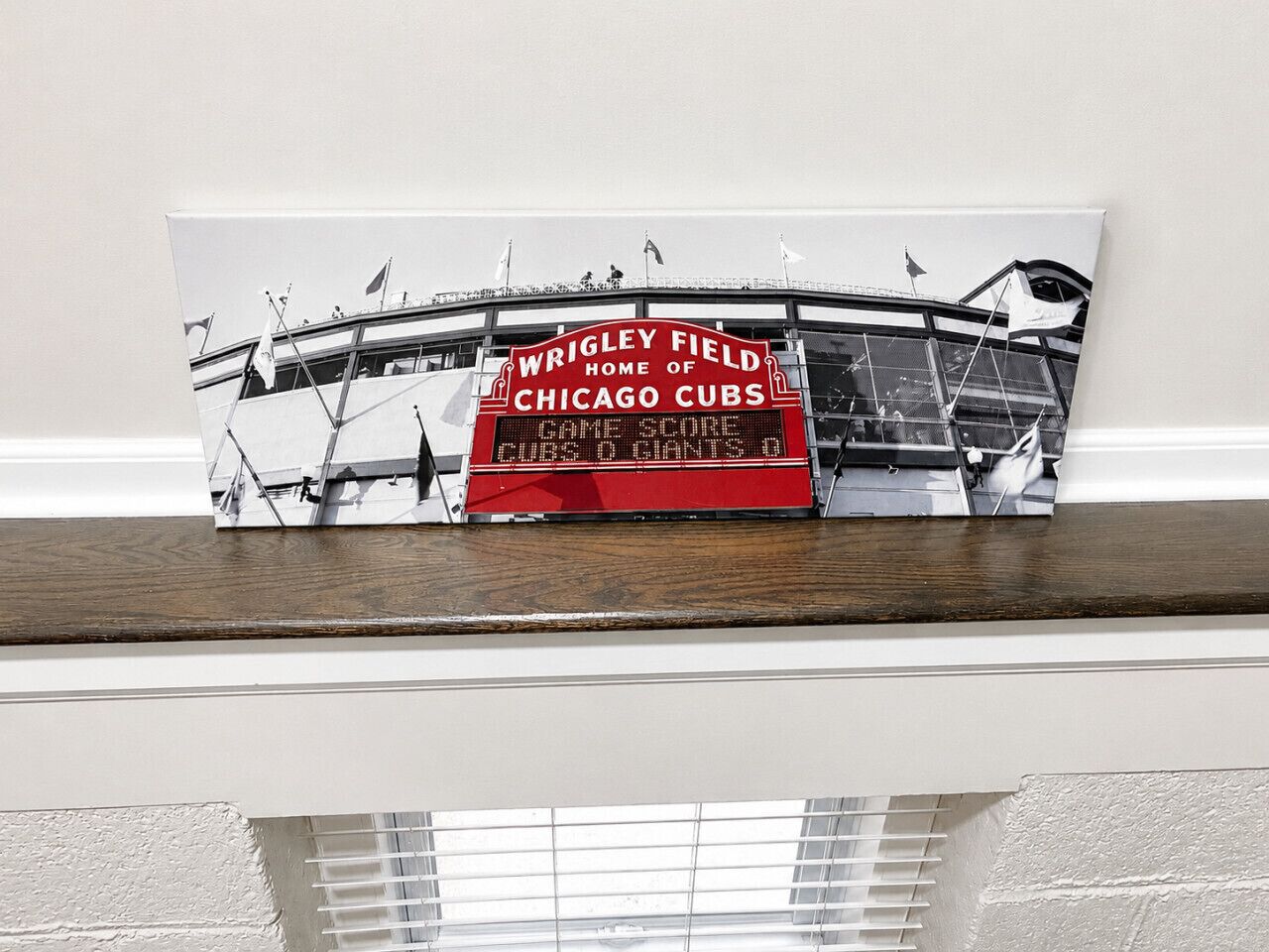 A framed picture of Wrigley Field with a scoreboard reading 'CUBS 0 GIANTS 0' on a shelf.