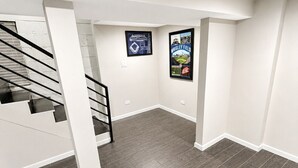 Une pièce spacieuse avec un escalier, un parquet en bois foncé et deux affiches encadrées accrochées aux murs.