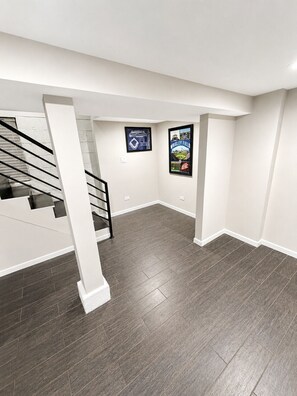 A spacious room with a staircase, dark wooden flooring, and two framed posters on the walls. - Welcome to this four bedroom, two bathroom apartment located in the neighborhood of Lakeview. (Chicago)