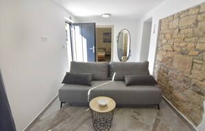 Ein modernes Wohnzimmer mit einem grauen Sofa, einem kleinen runden Tisch mit einer Schüssel, einer Steinwand und einer Tür zu einem weiteren Raum.