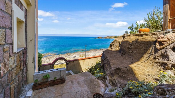 Vista costeira com um edifício de pedra, uma estrutura de madeira e uma saliência rochosa.