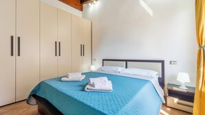 Quarto com cama, mesa de cabeceira, abajur e guarda-roupa.