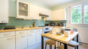A kitchen with white cabinets, a wooden countertop, a microwave, a stove, and a window with a view of trees. - Apartment “Ty Heol – Balcony and Near Center” with Balcony and Wi-Fi (Quimper)
