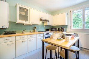 Una cocina con armarios blancos, encimera de madera, microondas, estufa y ventana con vistas a árboles.