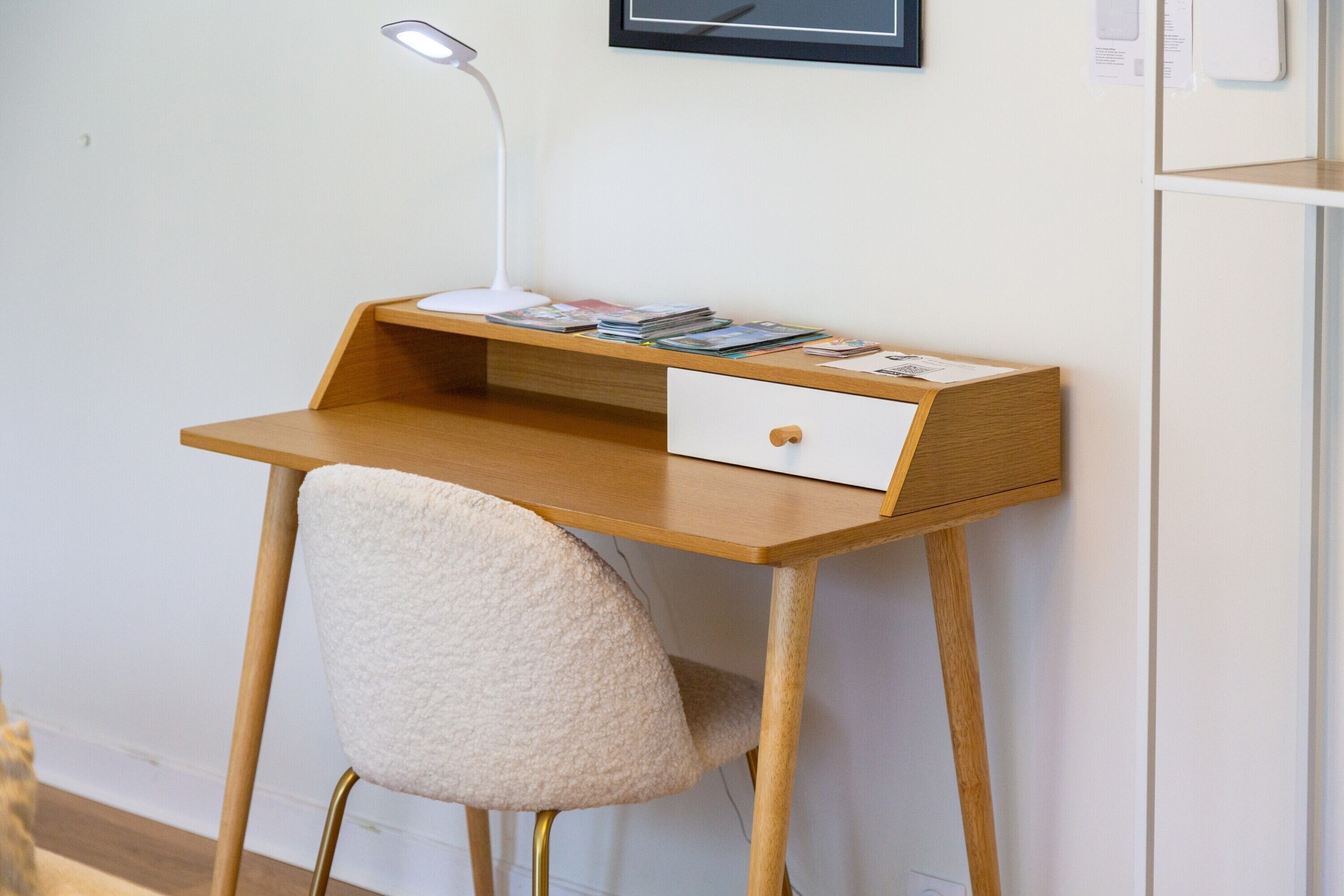 A wooden desk with a white chair, a desk lamp, and some magazines.
