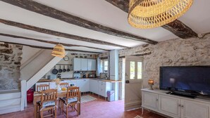 A rustic kitchen with exposed beams, a dining area with wooden chairs, and a television on a cabinet.