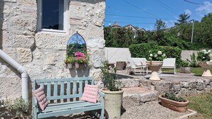 A stone building with a window, a bench with a cushion, and potted plants.