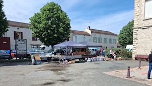 A street market with a tent, parked cars, and buildings in the background.
