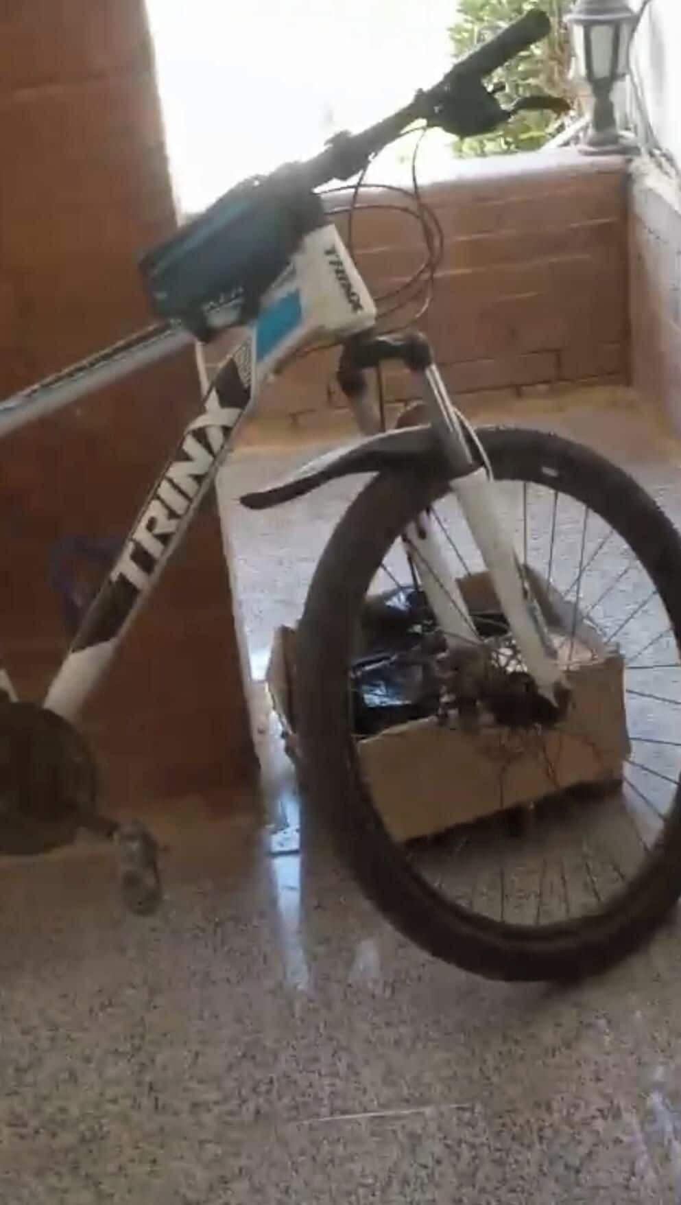 Bicicleta estatica amb un nom de marca visible, situada a l'interior amb un terra de rajoles i una paret de maó al fons.