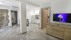 A modern living room with a flat-screen TV, a stone accent wall, and a minimalist kitchen in the background. - Relaxing Stay in a Homey Flat (Buje)