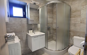 Een moderne badkamer met een douchecabine van glas, een wit wastafelmeubel en een toilet.