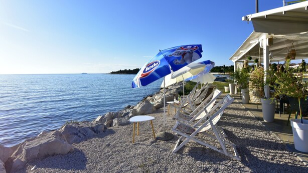A beachside area with pebbled ground, lounge chairs, and umbrellas. - Relaxing Stay in a Homey Flat (Buje)