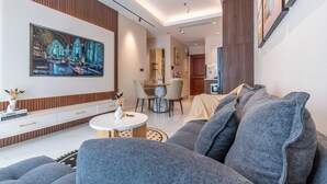 Uma sala de estar moderna com uma televisão de tela plana grande, sofás cinzentos, uma mesa de centro redonda e uma área de jantar com uma mesa pequena e cadeiras.