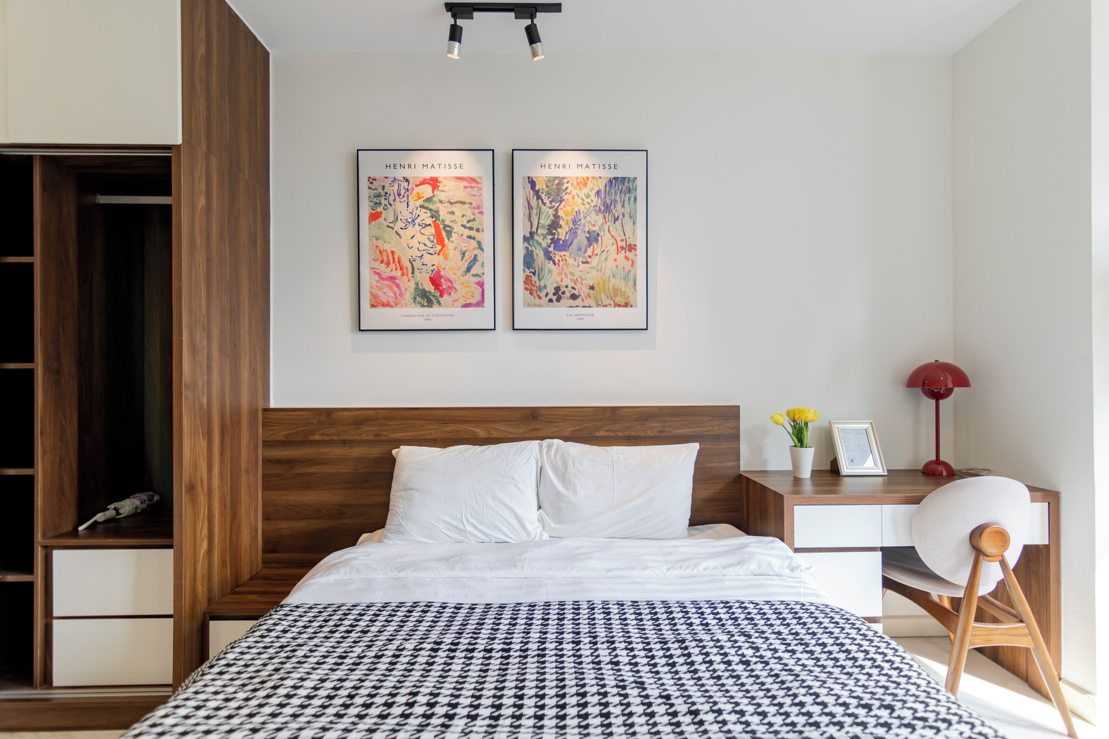 Ein modernes Schlafzimmer mit einem Holz-Kopfteil, einer houndstooth-Bettdecke, einem Nachttisch mit Lampe und zwei gerahmten Kunstwerken an der Wand.