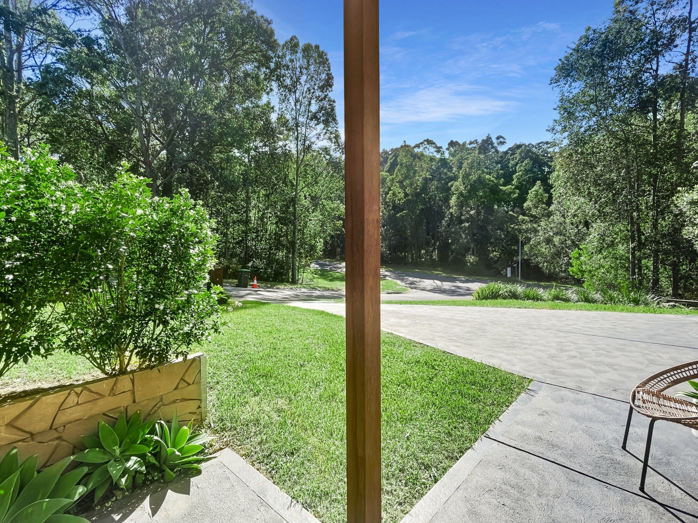 A paved pathway leading to a wooded area with a grassy lawn and a bench.