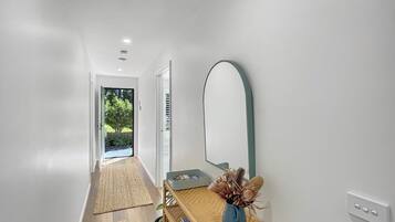 A hallway with a wooden floor, a woven rug, a small table with a vase, and a large mirror on the wall.