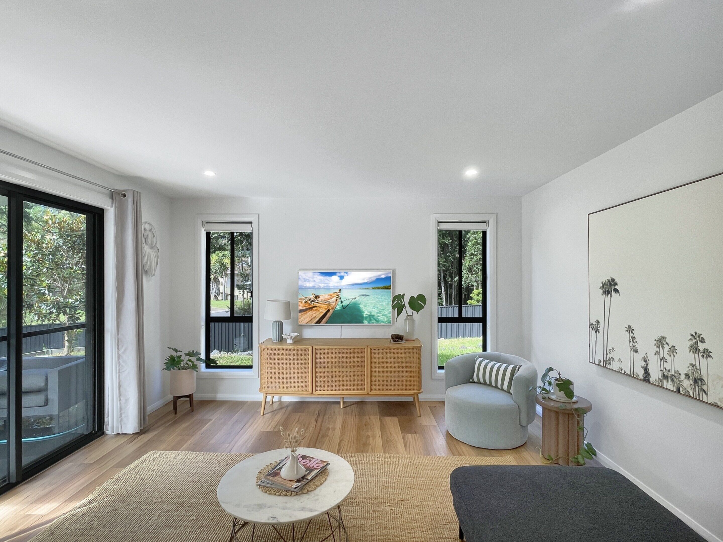 A modern living room with a wooden cabinet, a round coffee table, a grey armchair, and a large painting on the wall.