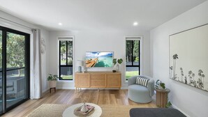 Uma sala de estar moderna com um armário de madeira, uma mesa de centro redonda, uma poltrona cinza e um quadro grande na parede.