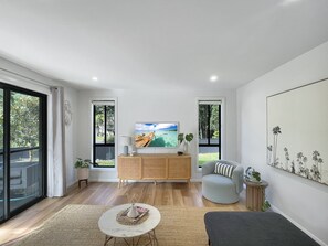 Ein modernes Wohnzimmer mit einem Holzkasten, einem runden Couchtisch, einem grauen Sessel und einem großen Gemälde an der Wand.