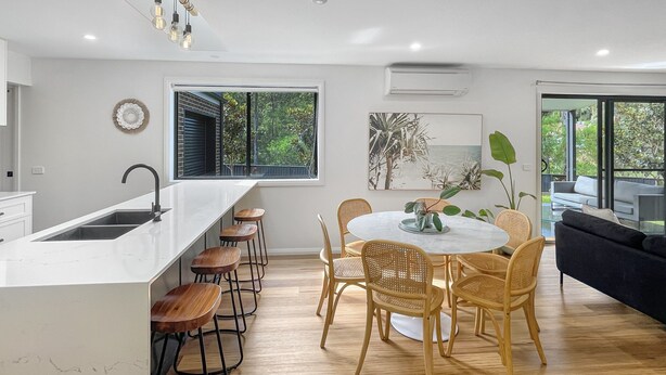 Cozinha moderna com ilha central, banquetas, mesa de jantar com cadeiras e uma janela grande com vista para o verde.