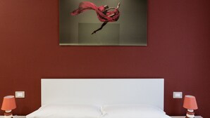 Un llit amb roba blanca, una paret vermella i una pintura d'una ballarina.