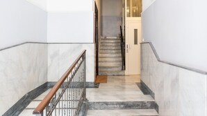 Gradi marbresos amb barana de fusta i baranetes metàl·liques, que condueixen a una porta amb interruptor de llum i un llum fixat a la paret.