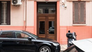 Un edifici amb una porta marró i persianes, un cotxe negre aparcat i una moto.