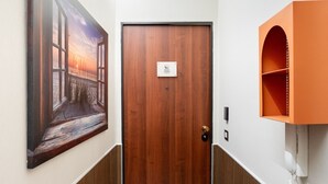 Habitació d'hotel amb una porta de fusta, un quadre del capvespre, un telèfon i un moble prestatge.