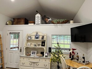 A living room with a TV, a Christmas tree, a wooden table with bottles, and a white cabinet with drawers.