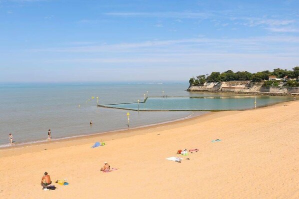 A beach with people, a pier, and a cliff with vegetation. - Le Petit Boyard – swimming pool, family and beach (Fouras)