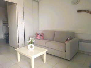 A living room with a sofa, a small table with a vase, and a door leading to another room. - Le Petit Boyard – swimming pool, family and beach (Fouras)
