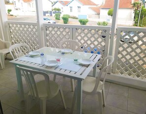 A table set for four with white chairs, a white tablecloth, and a view of houses through a lattice fence. - Le Petit Boyard – swimming pool, family and beach (Fouras)