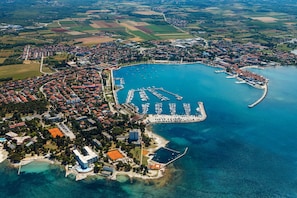 Vista aérea de un pueblo costero con un puerto deportivo, zonas residenciales y campos circundantes.