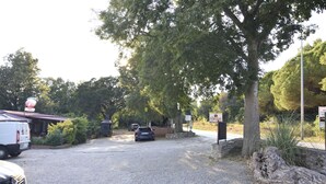 A gravel driveway leading to a building with a signboard, a parked car, and a white van. - Lovely Apartment for a Comfortable Stay (Buje)