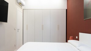 A bedroom with a bed, a wardrobe, a television mounted on the wall, and a red accent wall. - Almarea Suites Levante by Wonderful Italy (Bari)