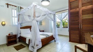 A bedroom with a four-poster bed, a wooden wardrobe, a bedside table, and a window with curtains. - Taraji Suites Diani (Diani Beach)